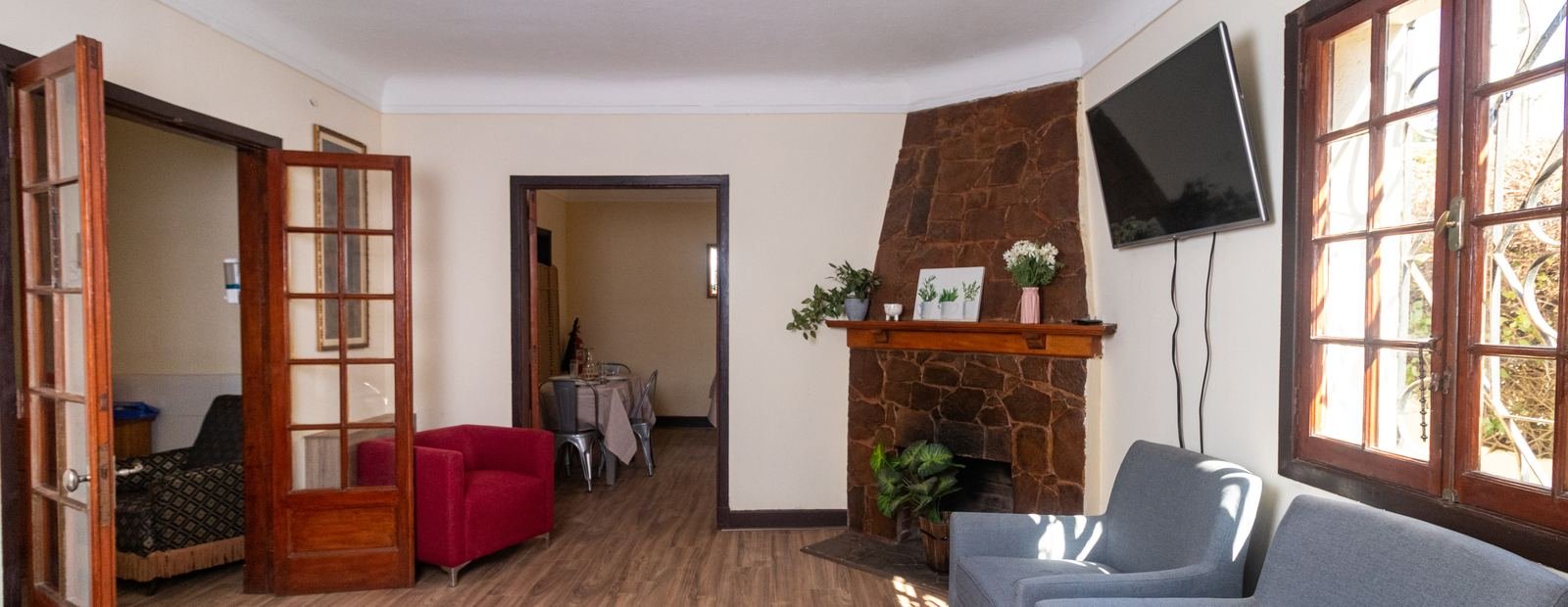 Sala de estar con chimenea de piedra, sillones y las puertas abiertas hacia el comedor.